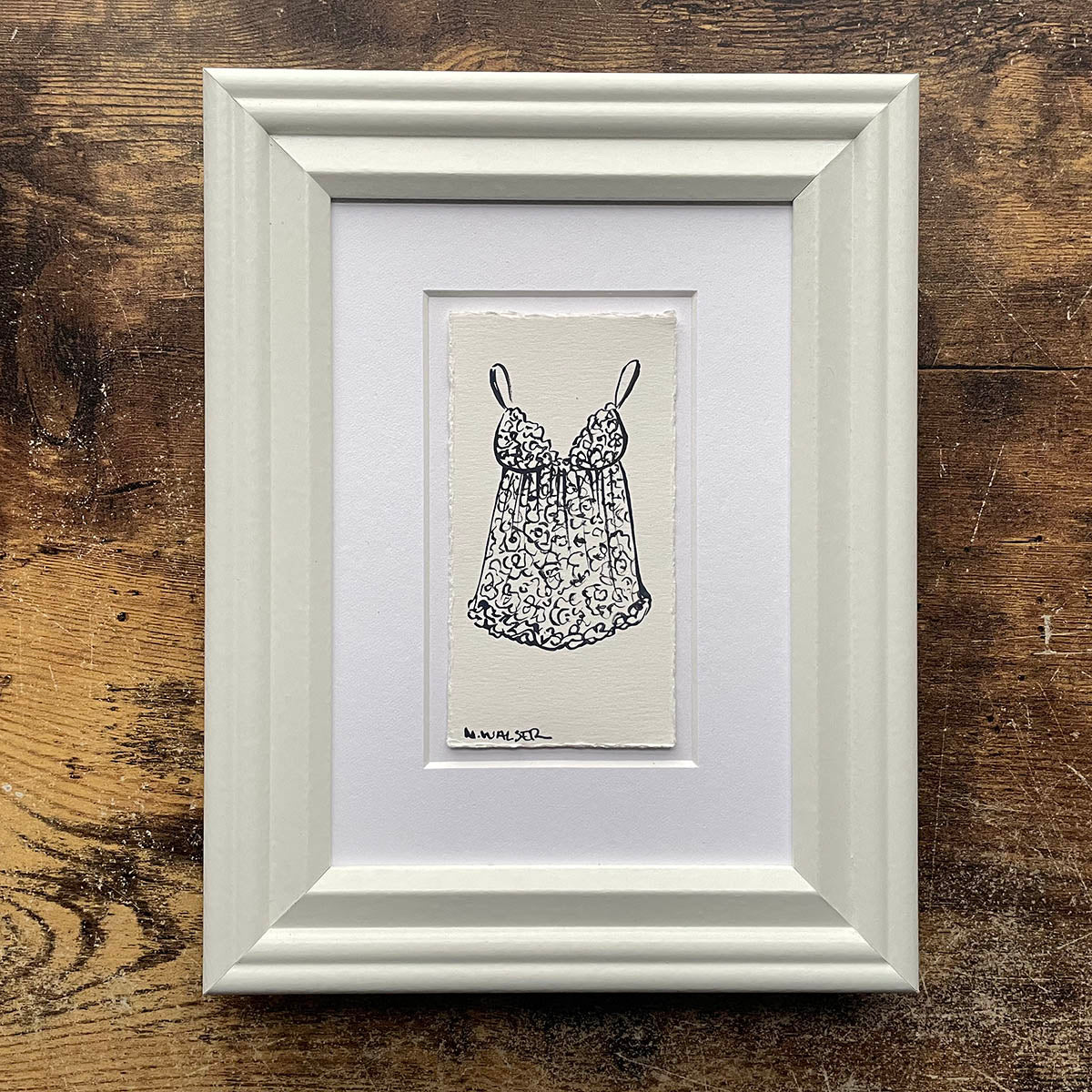 Framed artwork of a lace slip dress on a wooden surface