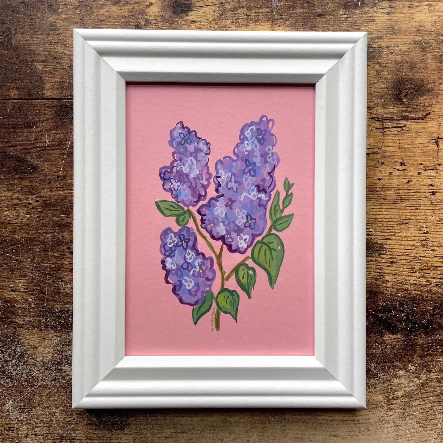Framed artwork of purple lilac flowers on a pink background