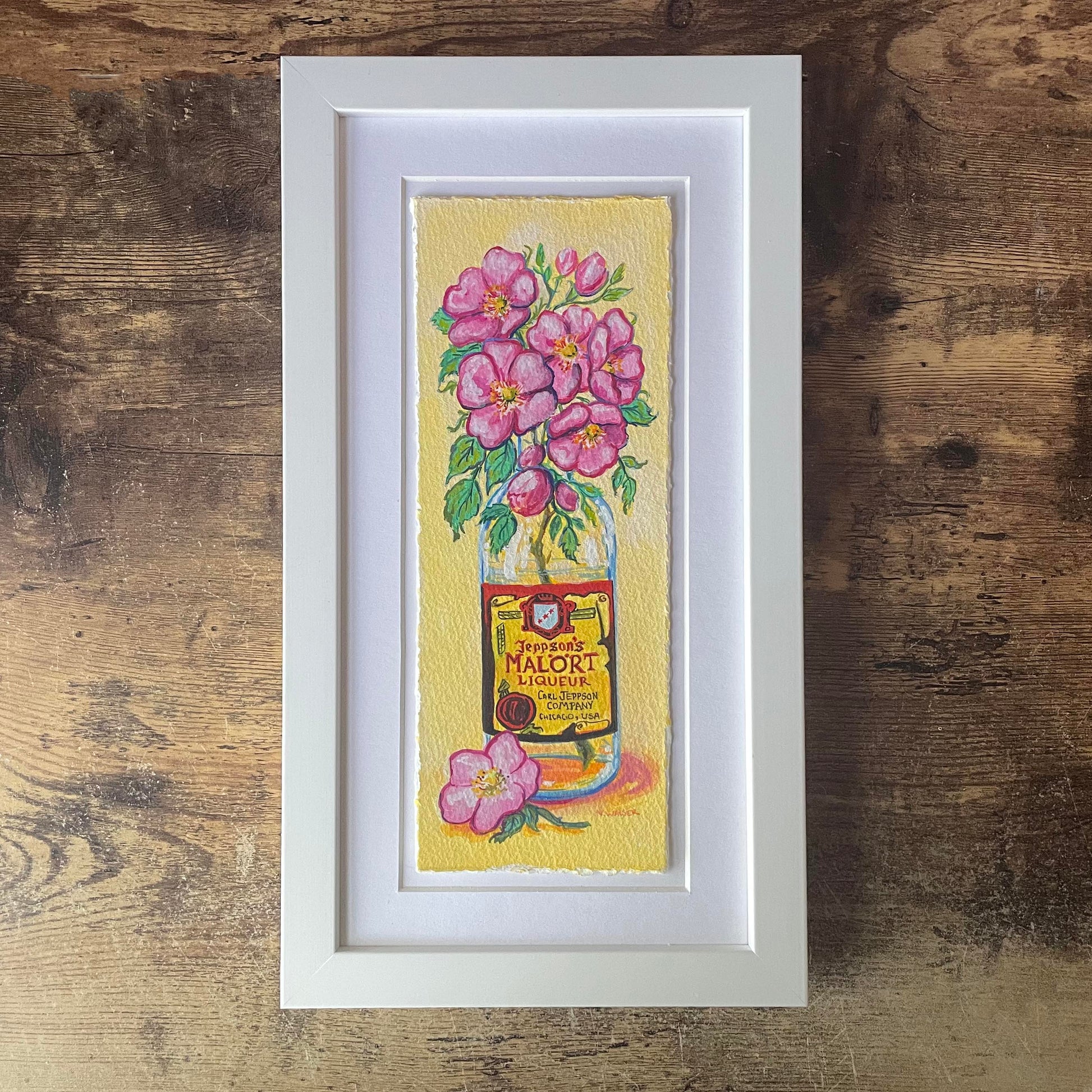 Framed artwork of a Malort bottle with pink flowers on a yellow background