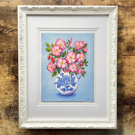 Framed artwork of a vase with pink rose flowers and blue patterns on a wooden surface