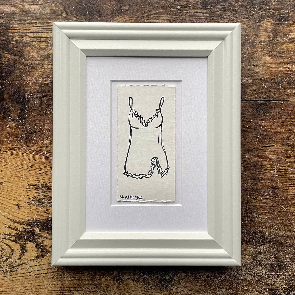 Framed black and white illustration of a dress on a wooden surface