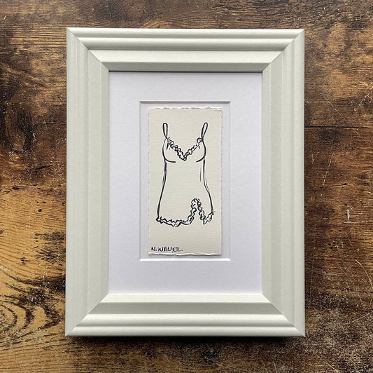 Framed black and white illustration of a dress on a wooden surface