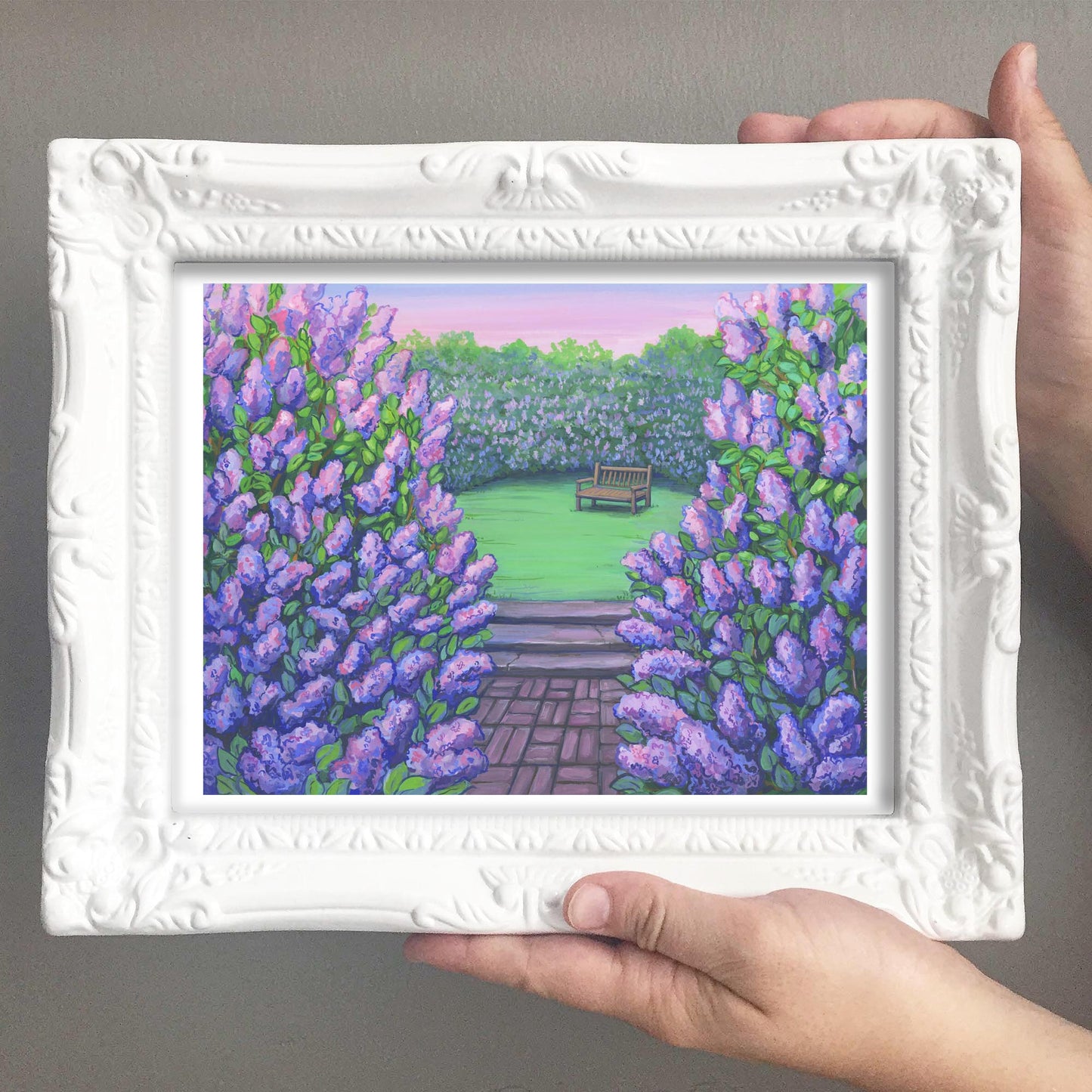 Framed artwork of a garden scene with purple lilac flowers and a bench.