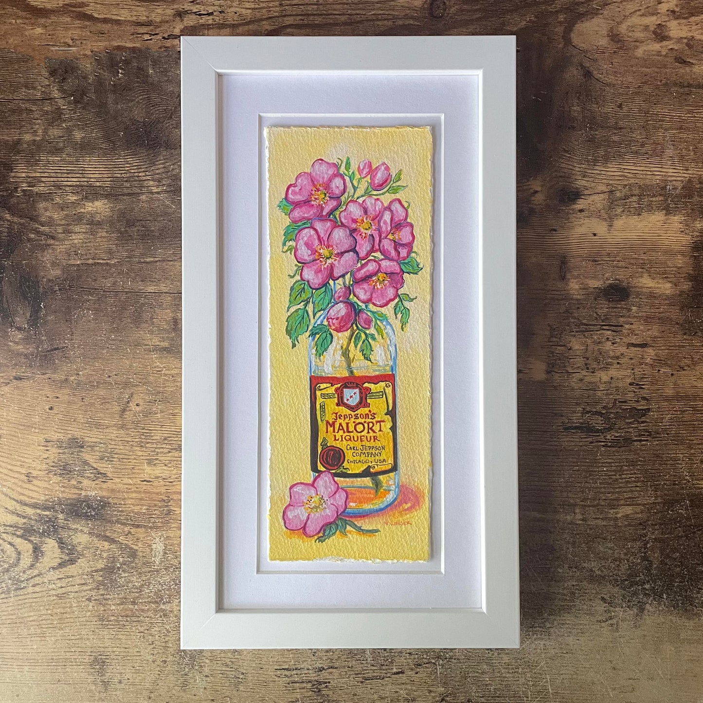 Framed artwork of a Malort bottle with pink flowers on a yellow background