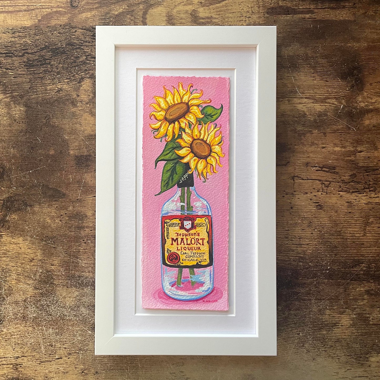Framed artwork of sunflowers in a Malort bottle on a pink background