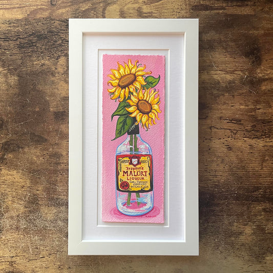Framed artwork of sunflowers in a Malort bottle on a pink background