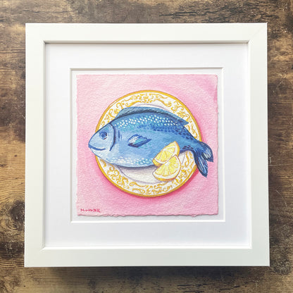 Framed artwork of a blue fish on a pink background with a white frame.