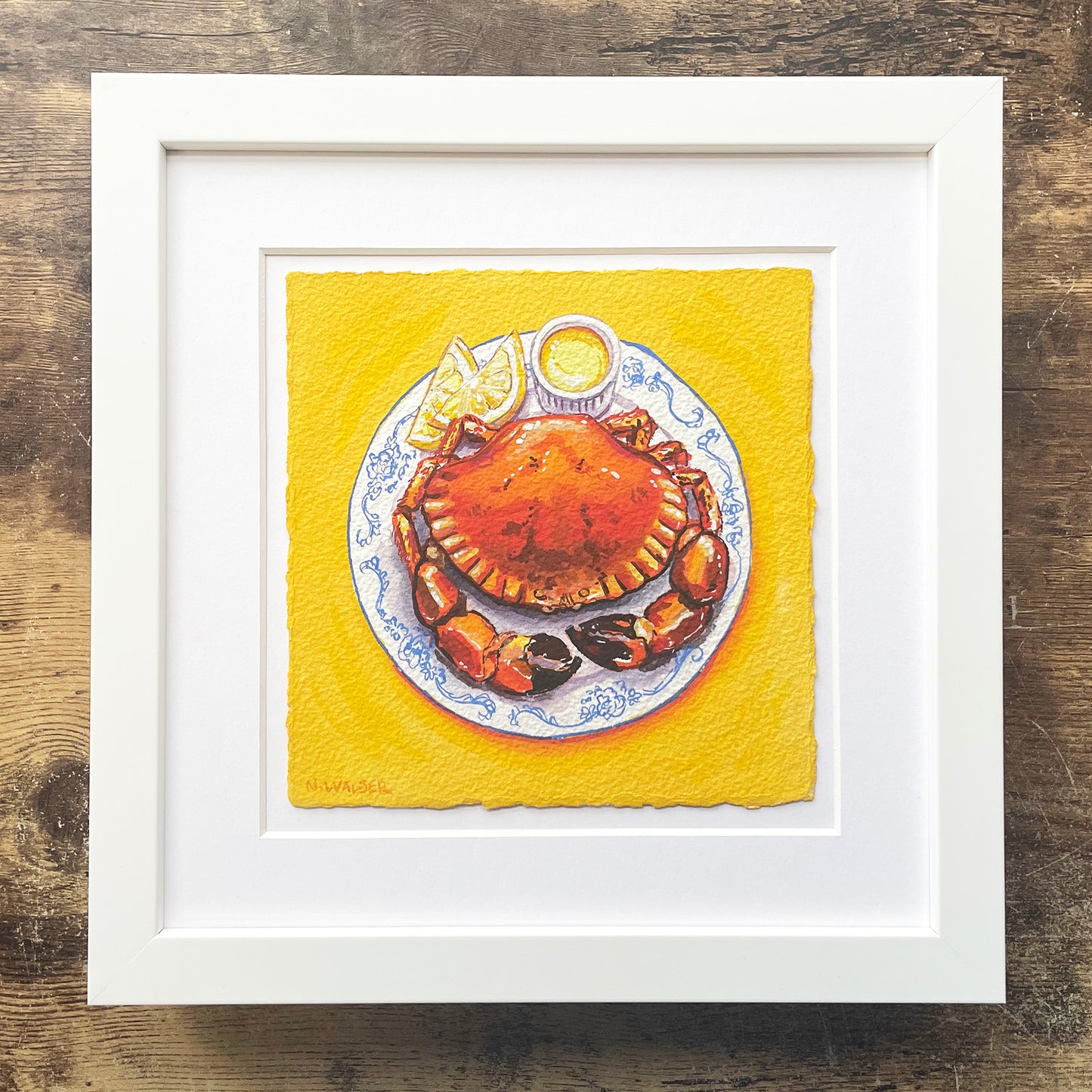 Framed artwork of a crab on a plate with lemon wedges on a yellow background