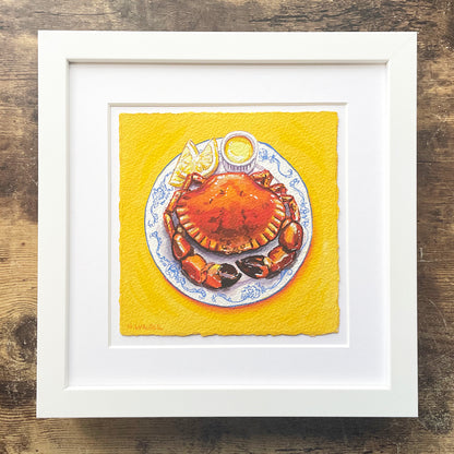 Framed artwork of a crab on a plate with lemon wedges on a yellow background