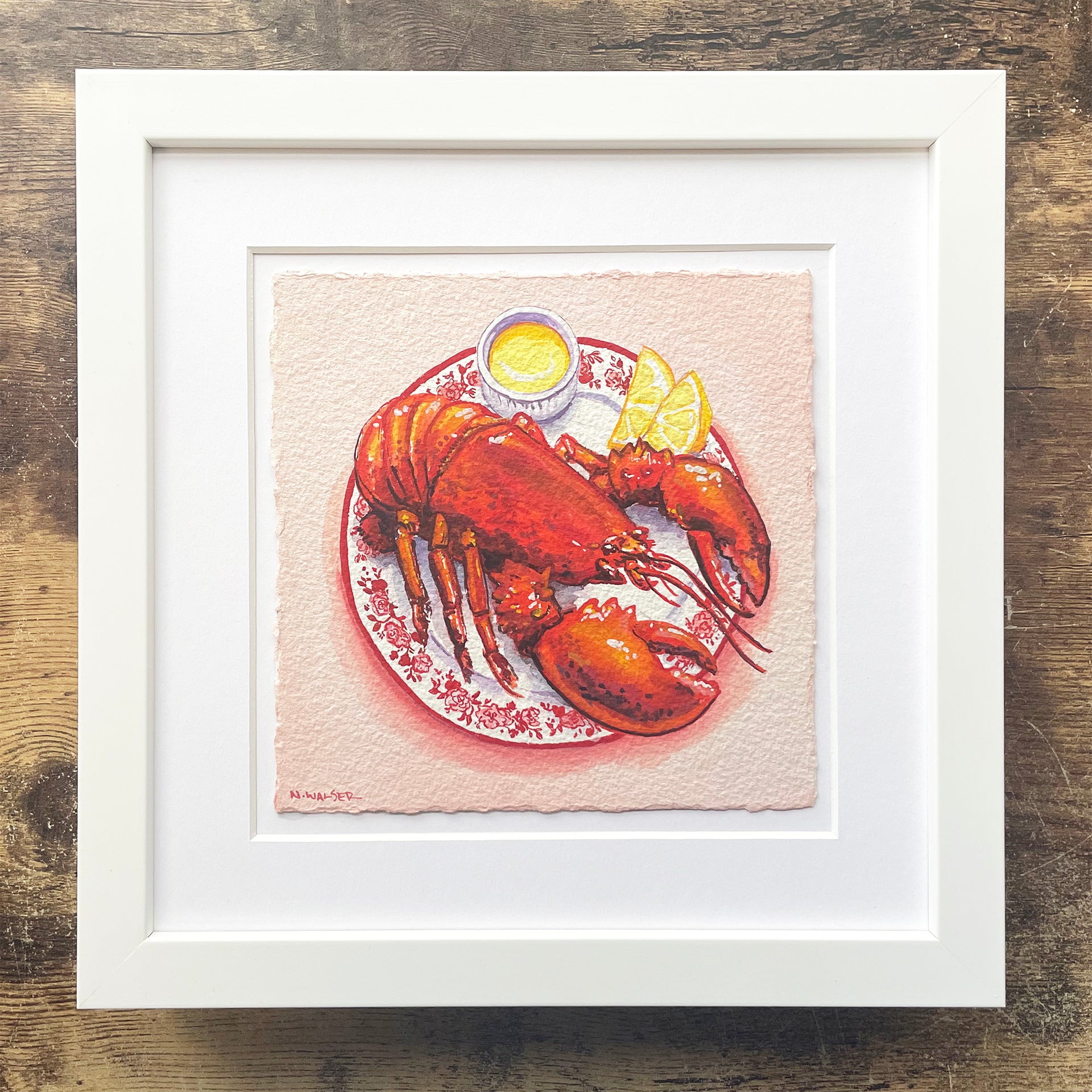 Framed artwork of a lobster on a plate with a lemon wedge and butter dish.